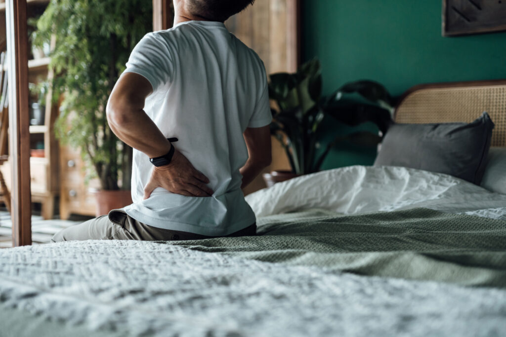 Rear view of senior Asian man suffering from backache, massaging aching muscles while sitting on bed. Elderly and health issues concept
