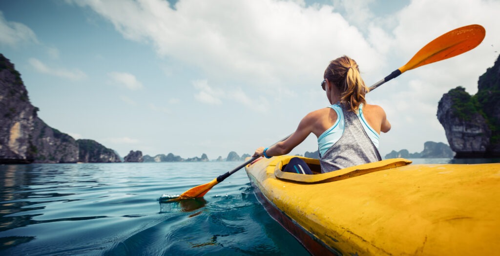 Woman exploring calm tropical bay with limestone mountains by kayak.