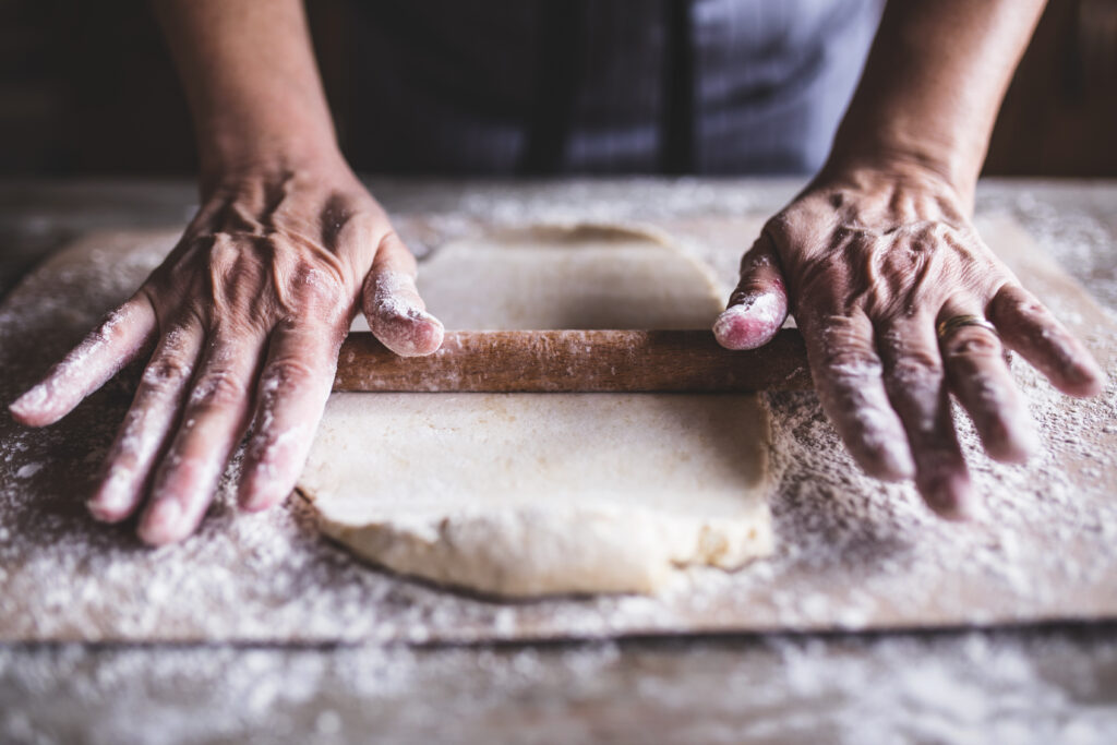 Hands baking dough with rolling pin on wooden table